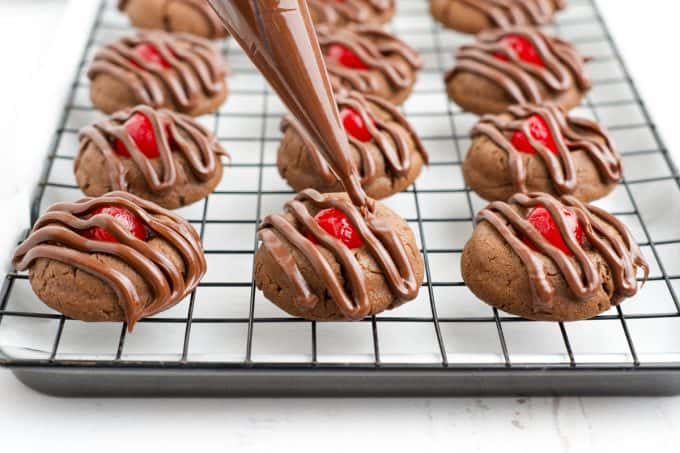 Piping chocolate onto cherry thumbprint cookies.
