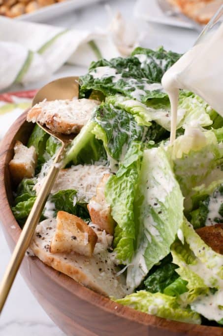 Pouring Caesar dressing over chicken salad.