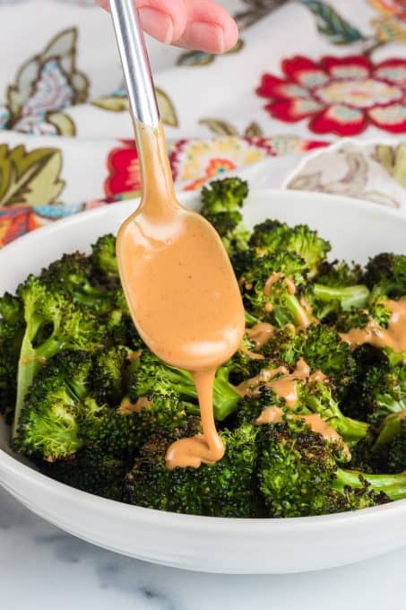 Drizzling a peanut butter sauce over roasted broccoli.