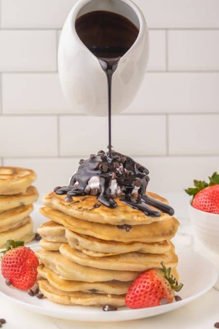 Pouring chocolate sauce over pancakes with chocolate chips.