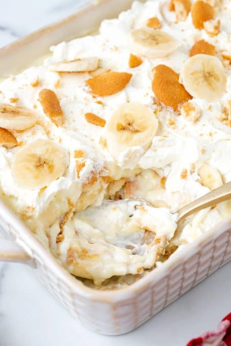 A dish of pudding with bananas, cookies and whipped cream.