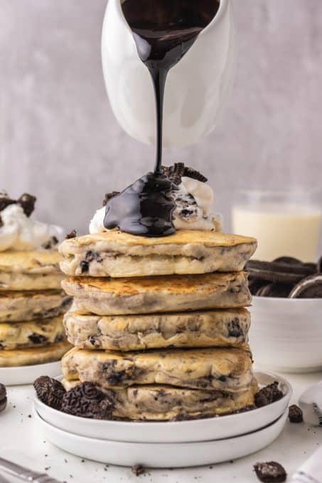 Drizzling chocolate sauce on a stack of pancakes.