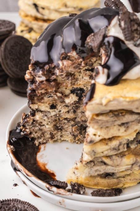 A stack of pancakes with Oreos, whipped cream and chocolate sauce.