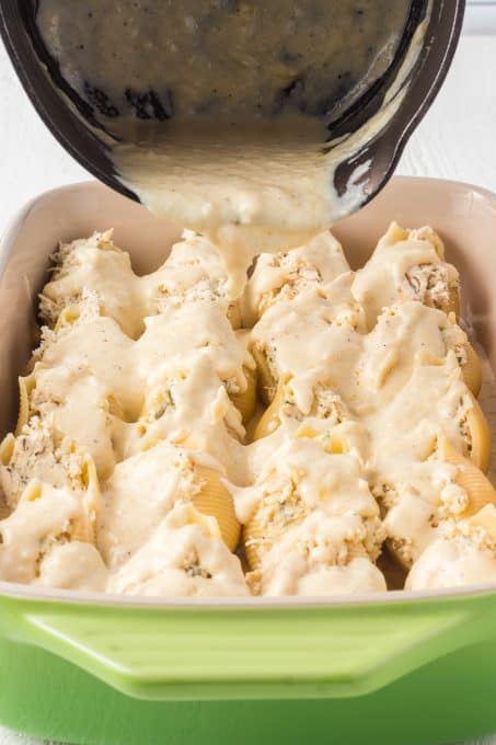 Pouring Garlic Alfredo Sauce over chicken stuffed shells