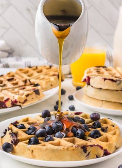 Pouring syrup on a waffle with blueberries.