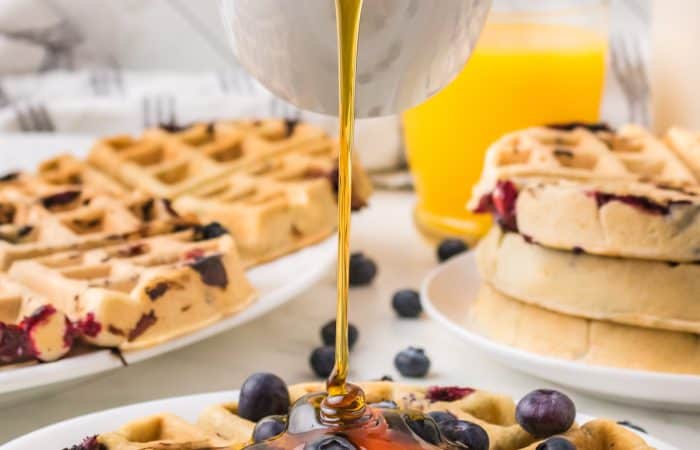 Pouring syrup on a waffle with blueberries.