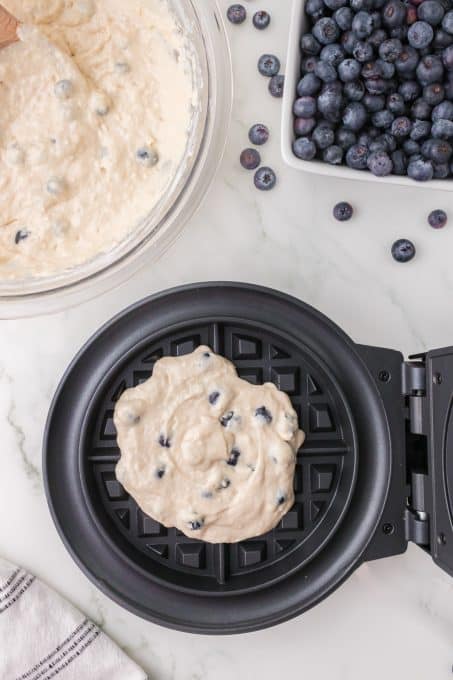 Putting blueberry batter into a waffle iron.