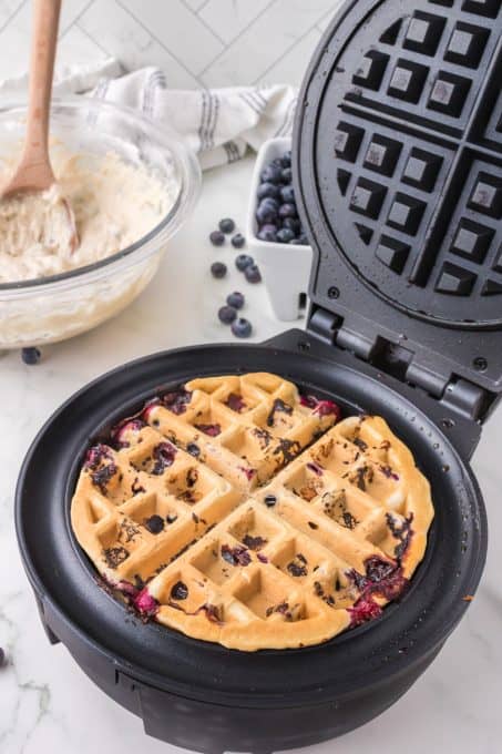 Cooking a blueberry waffle in a waffle iron.