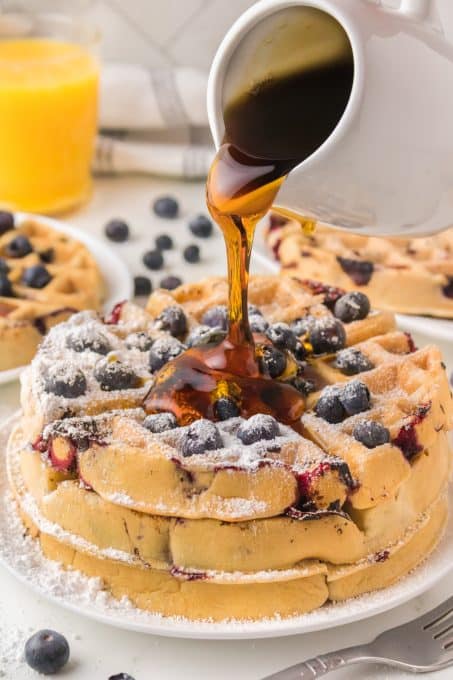 Syrup being poured on a stack of waffles made with blueberries.