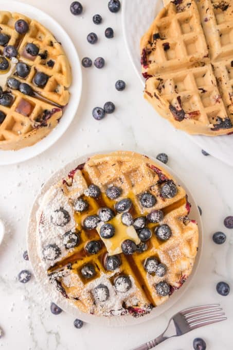 Powdered sugar, butter, and more blueberries on waffles with blueberries.
