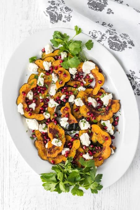 A plate of acorn squash with goat cheese, pomegranate arils and parsley.