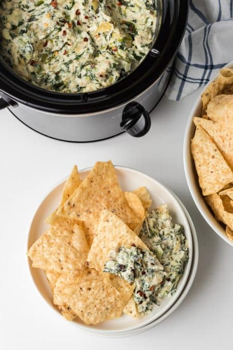 A slow cooker filled with a creamy spinach dip with artichokes.