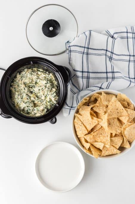 Chips, and spinach dip with artichokes in a crockpot.