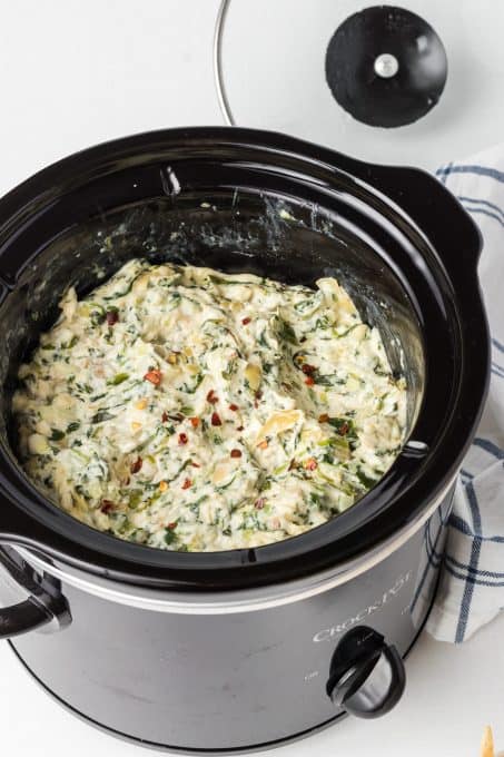 A slow cooker filled of an artichoke dip with spinach.