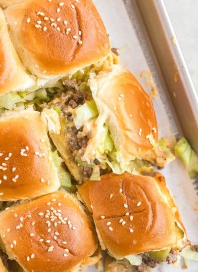 A slider with ground beef, lettuce, pickles, cheese and sauce.