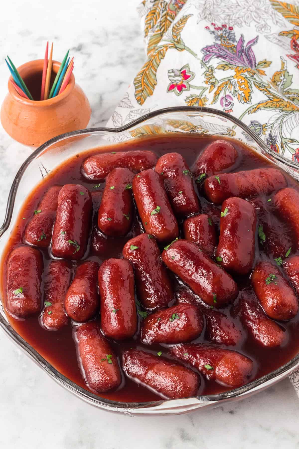 A bowl of cocktail sausages, toothpicks and a napkin.