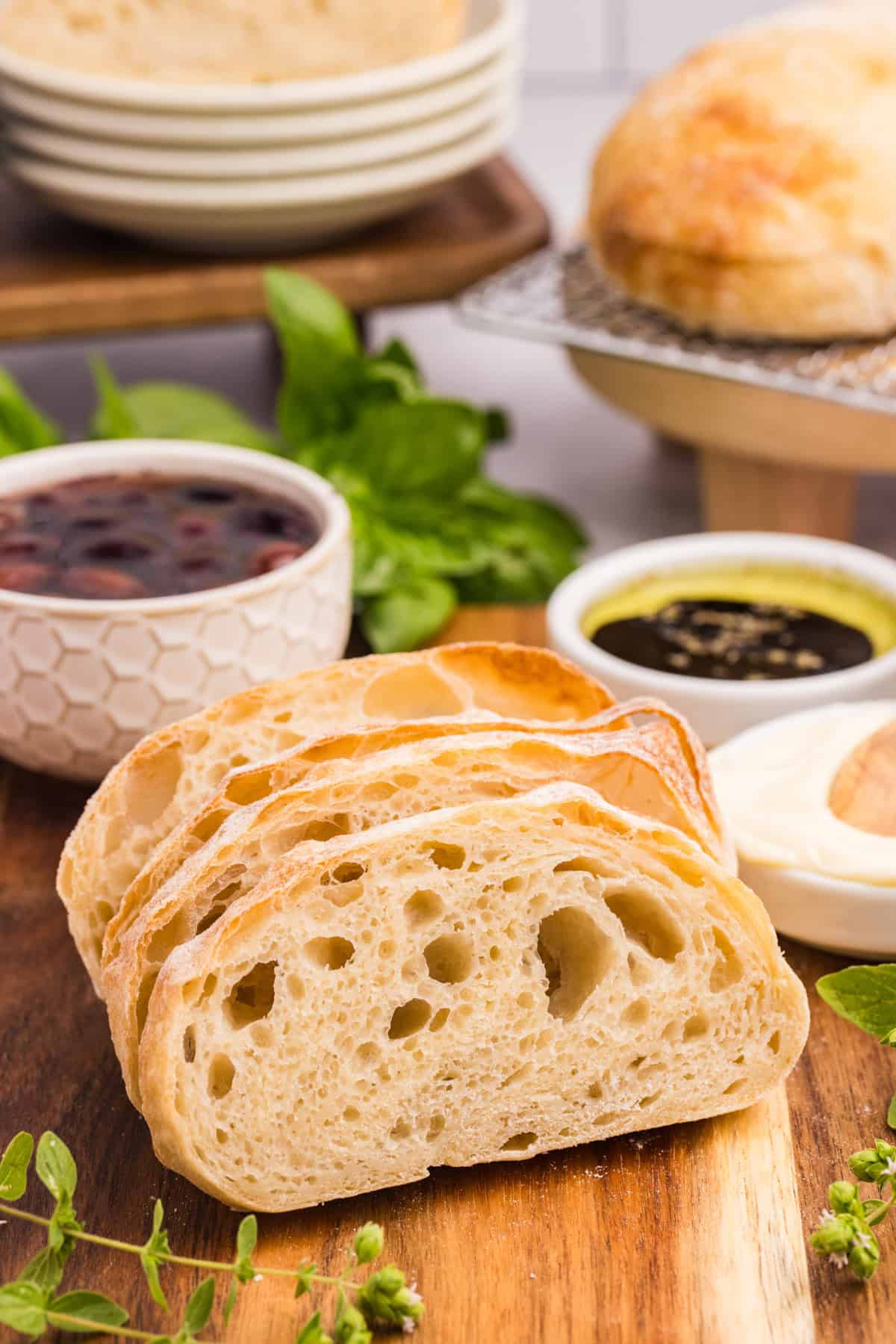 Slices of bread on a cutting board with a bowl of dipping sauce and a bowl of olives.