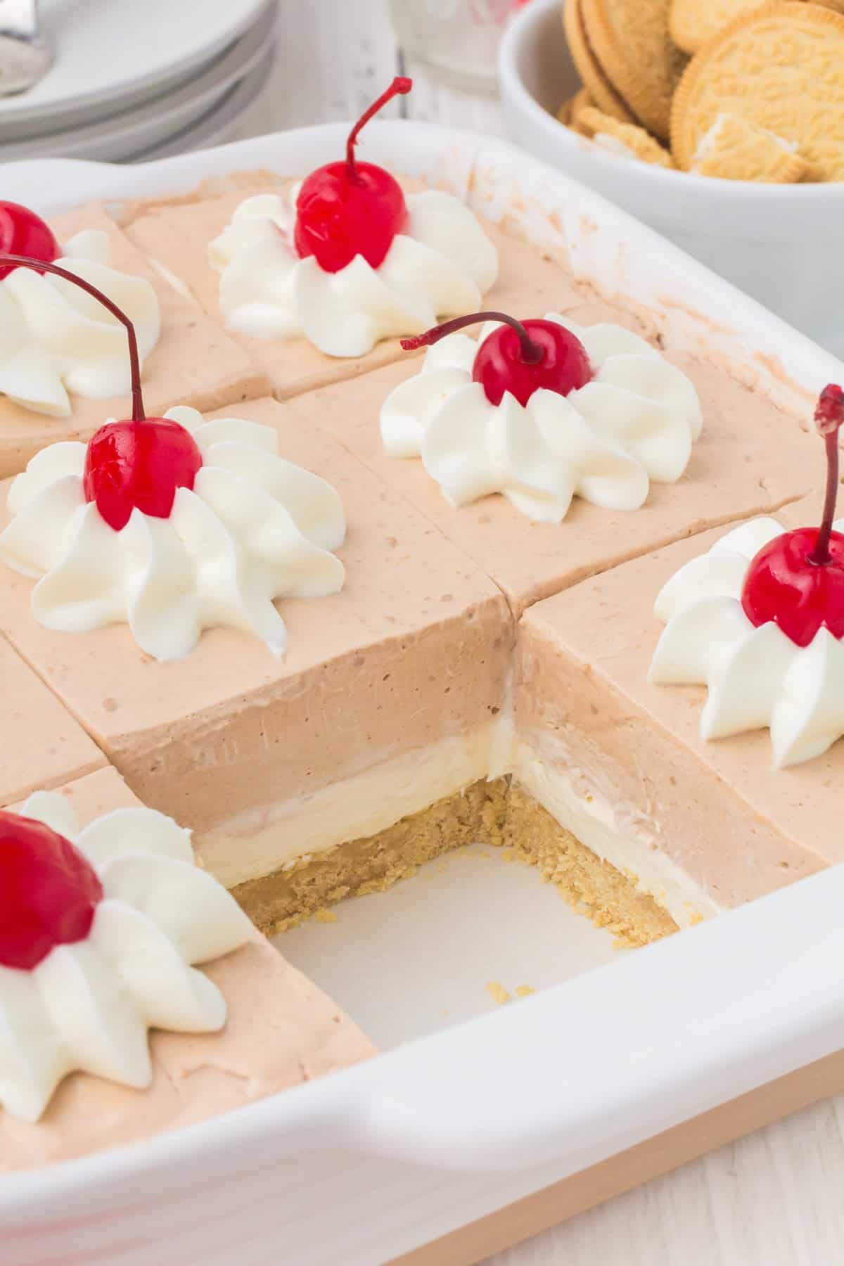 Looking into a pan with a slice taken out of Root Beer Dream Bars with whipped cream and cherries on top.