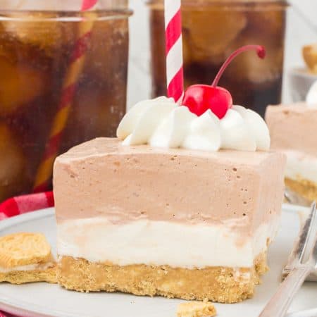 A layered dessert with whipped cream, a long stem cherry, and red and white drinking straw on top.