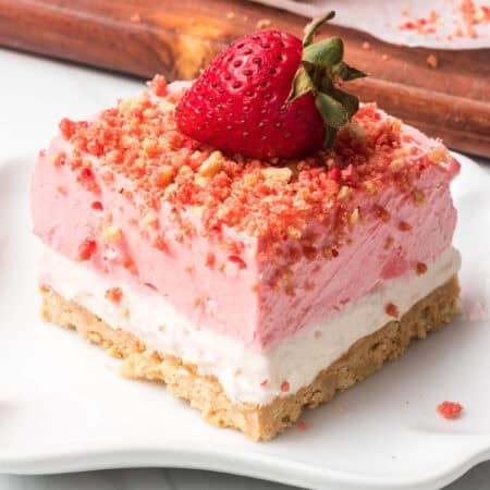 A no bake Strawberry Crunch Dream Bar on a white plate topped with a strawberry.