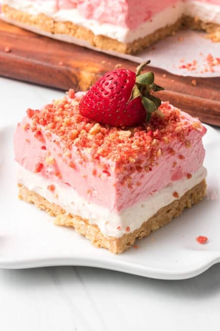 A no bake Strawberry Crunch Dream Bar on a white plate topped with a strawberry.