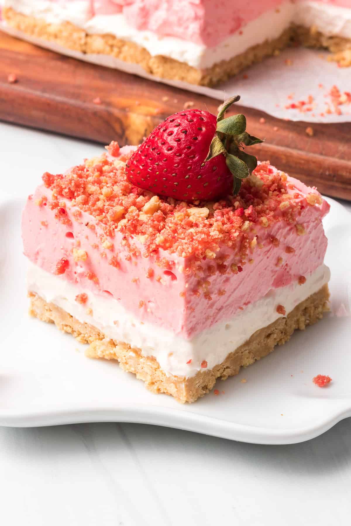 A no bake Strawberry Crunch Dream Bar on a white plate topped with a strawberry.