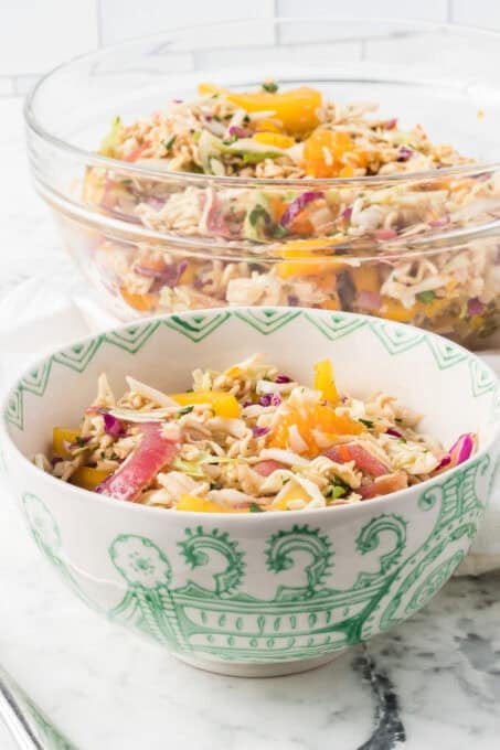 Bowls of coleslaw mix, mandarin oranges, chicken and pickled red onions mixed in a ginger dressing.