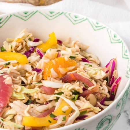 A bowl of an Asian inspired chicken salad with dry ramen noodles.