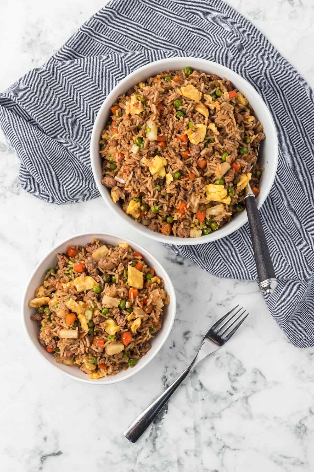Looking down at bowls full of ground pork, rice, carrots, peas, scrambled egg and pineapple.