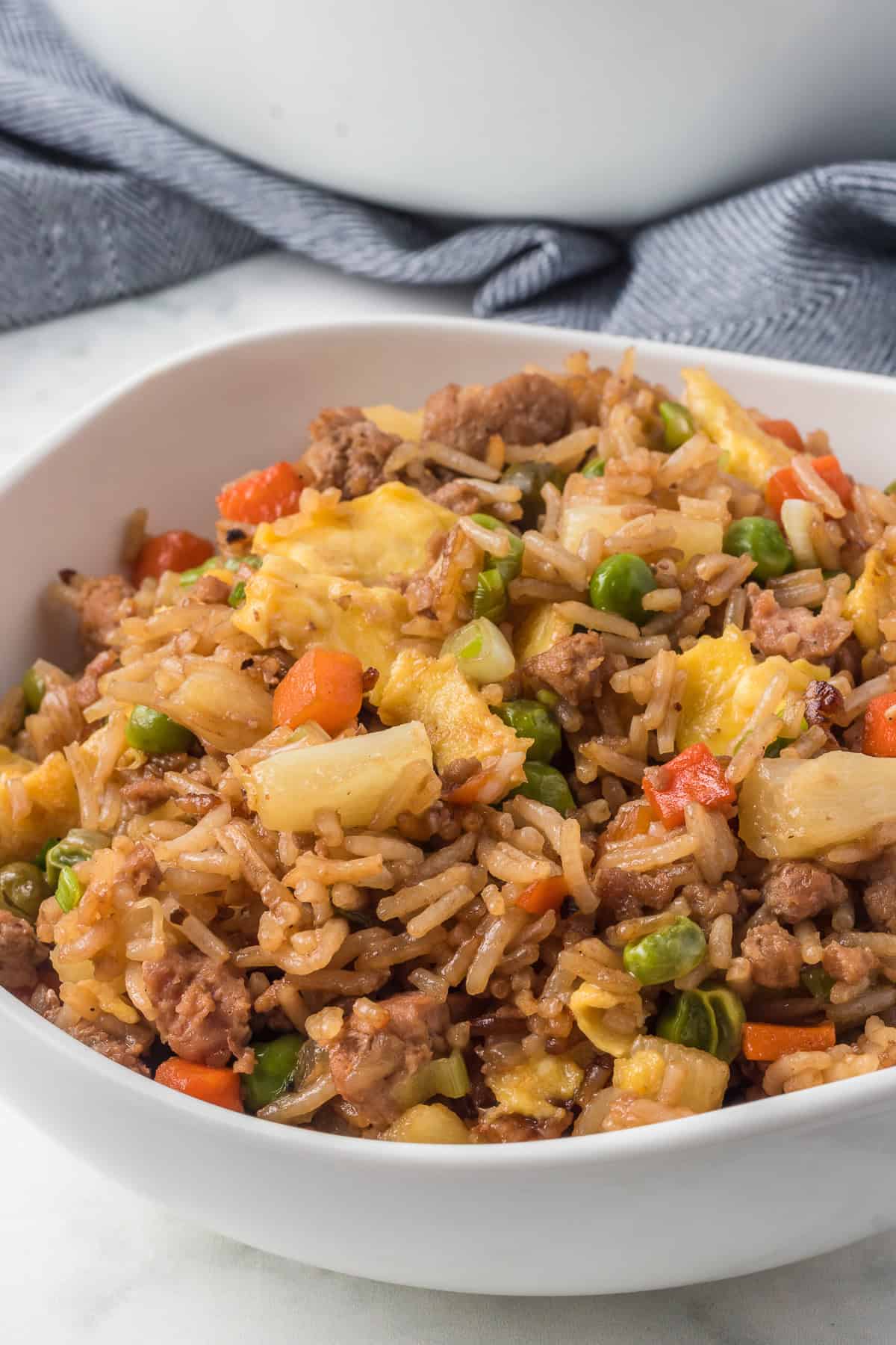 Rice, pineapple, ground pork, carrots, peas, and egg in a bowl.