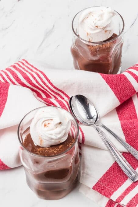 Two glasses with whipped cream and chocolate pudding with spoons and a red striped napkin.