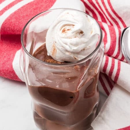 Whipped cream on a Dairy-Free Chocolate Pudding in a serving glass with a red striped napkin.