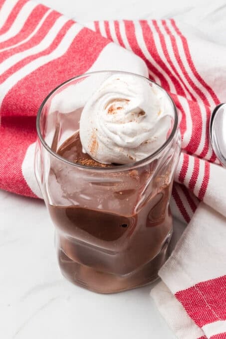 Whipped cream on a Dairy-Free Chocolate Pudding in a serving glass with a red striped napkin.