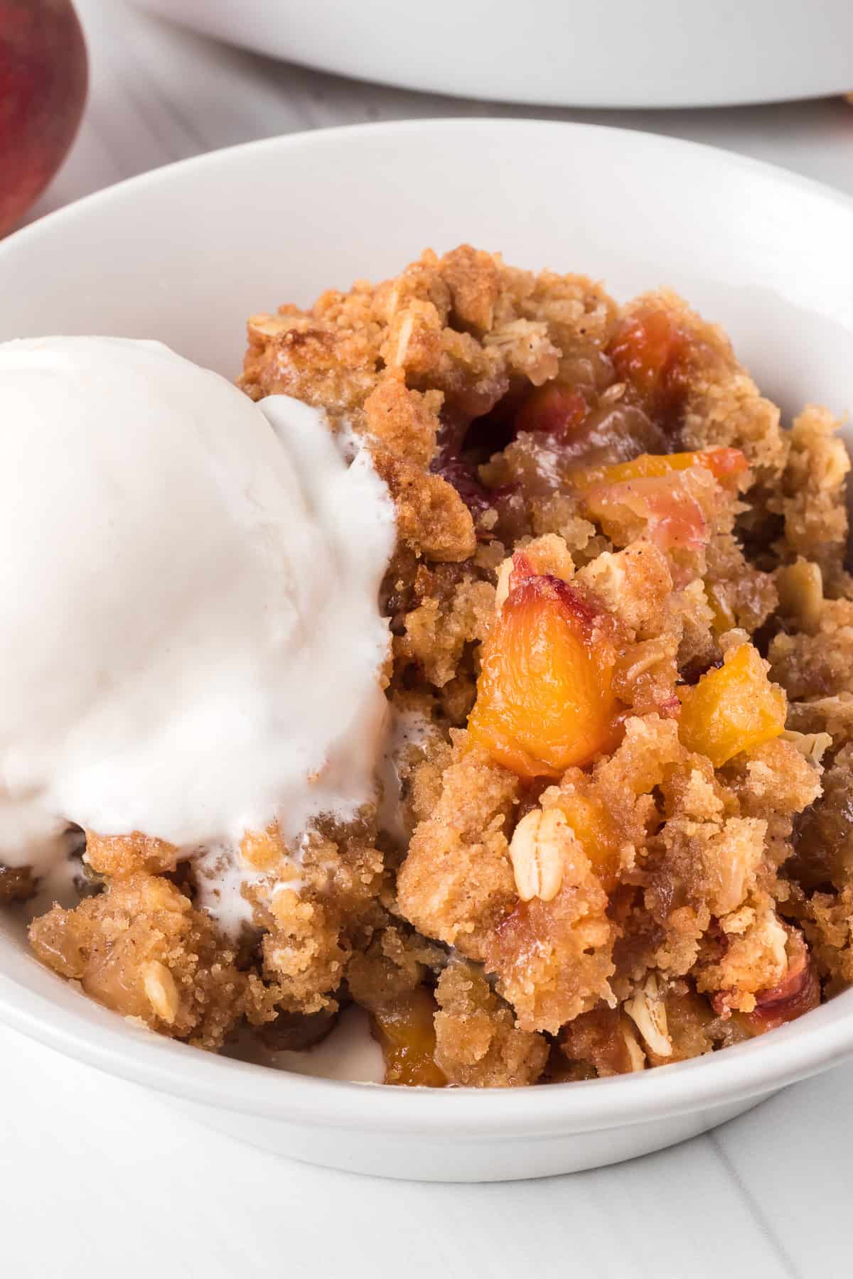 A scoop of vanilla ice cream on top of a peach dessert in a white bowl.