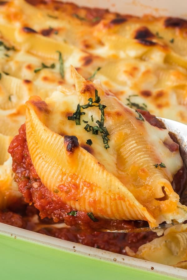 A stuffed shell on a spoon over a baking dish.