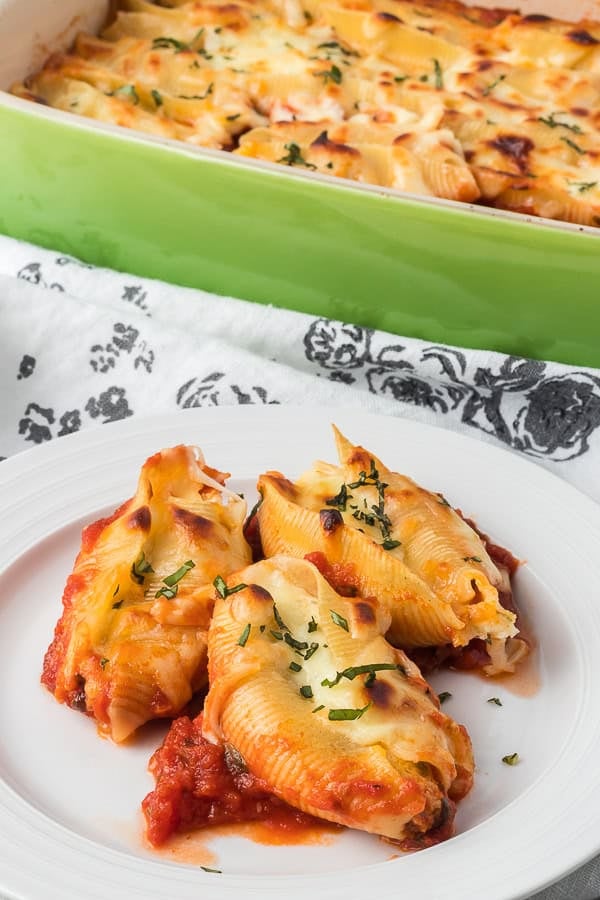 Three pasta shells on a plate stuffed with cheese.